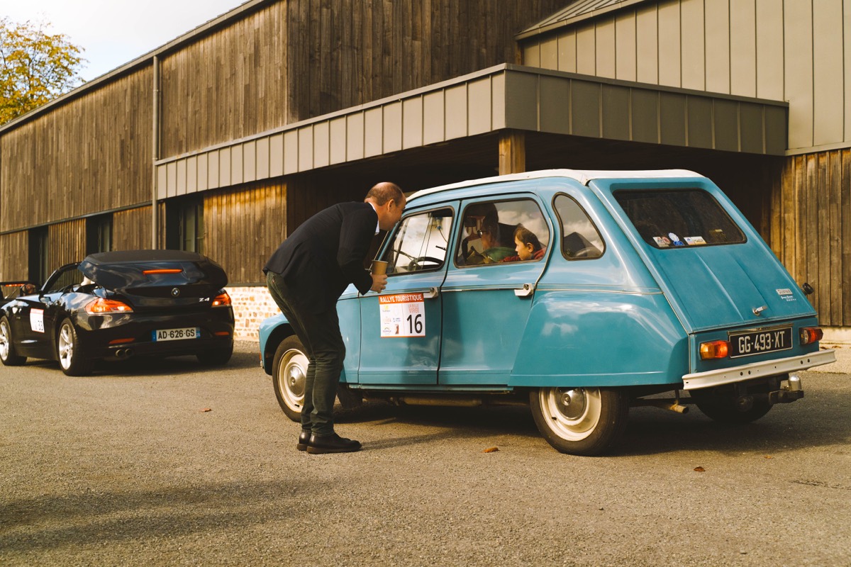 Participante saluant depuis une Citroën 2 CV turquoise